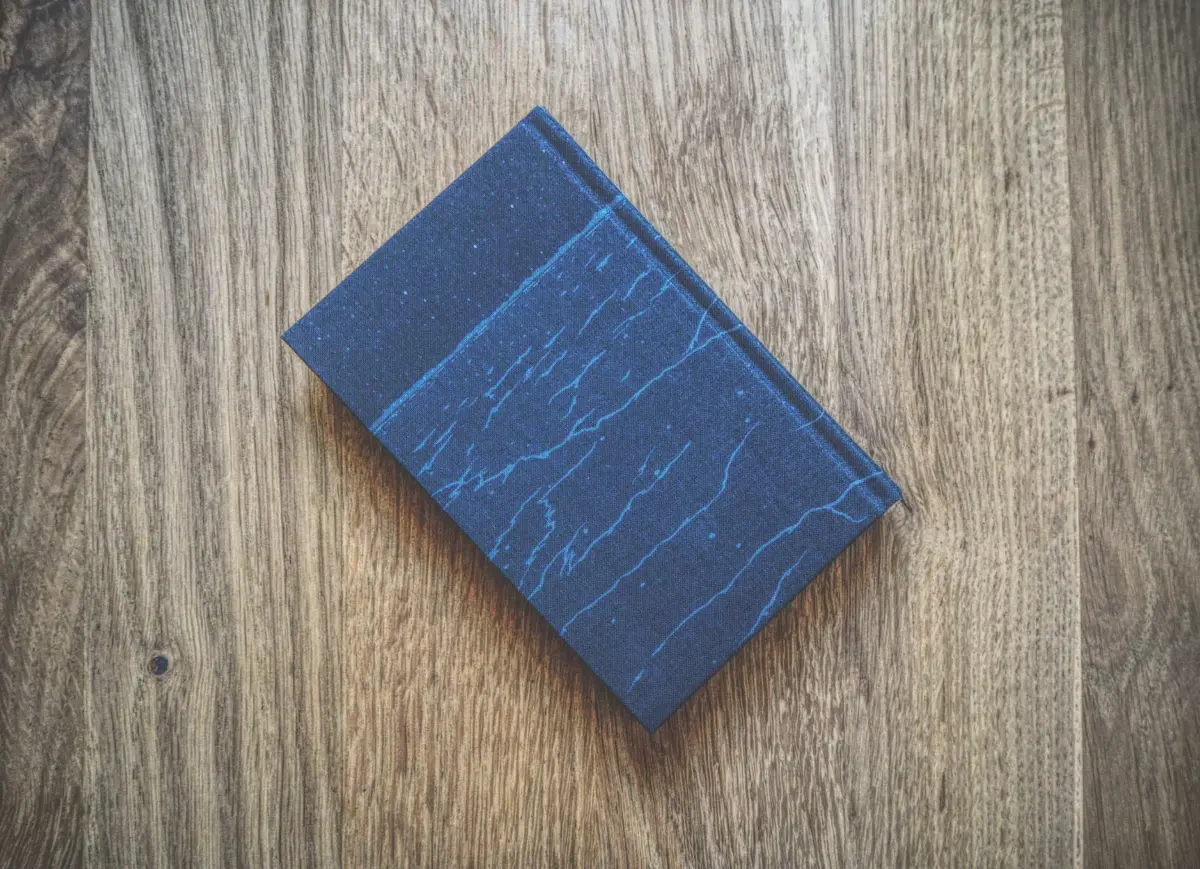 Auf einer Holzoberfläche liegt ein geschlossenes, dunkelblaues Hardcover-Buch mit marmorartigem Muster.