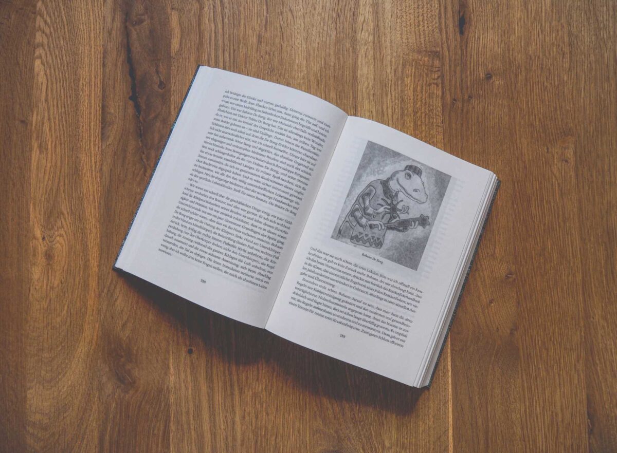 Ein auf einer Holzfläche aufgeschlagenes Buch zeigt auf beiden Seiten Text und auf der rechten Seite die Abbildung eines Frosches in Kleidung.