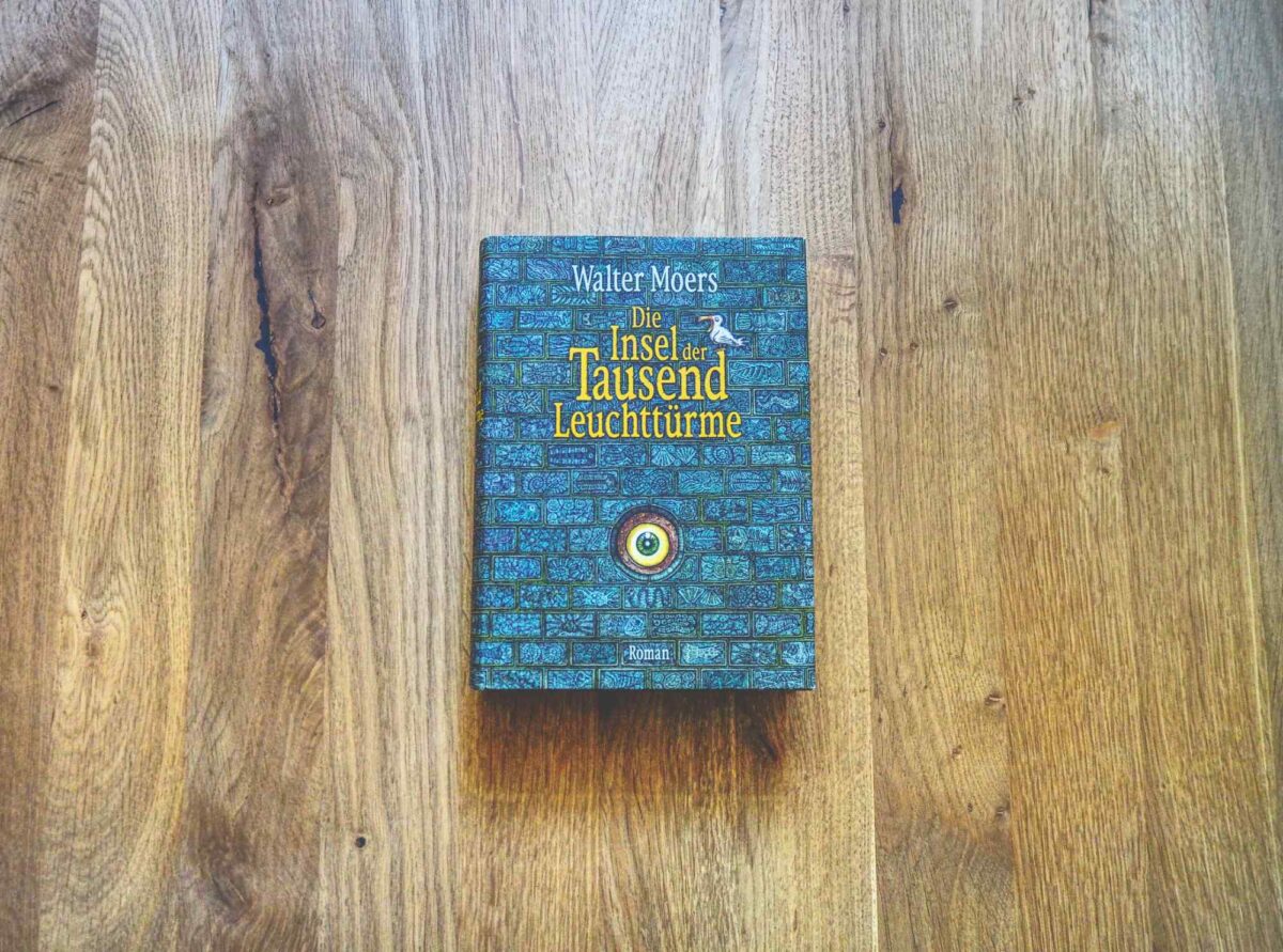 Ein Buch mit dem Titel „Die Insel der Tausend Leuchttürme“ von Walter Moers liegt in der Mitte einer Holzfläche.