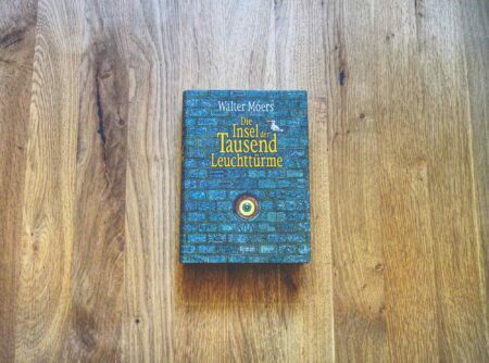 Ein Buch mit dem Titel „Die Insel der Tausend Leuchttürme“ von Walter Moers liegt in der Mitte einer Holzfläche.
