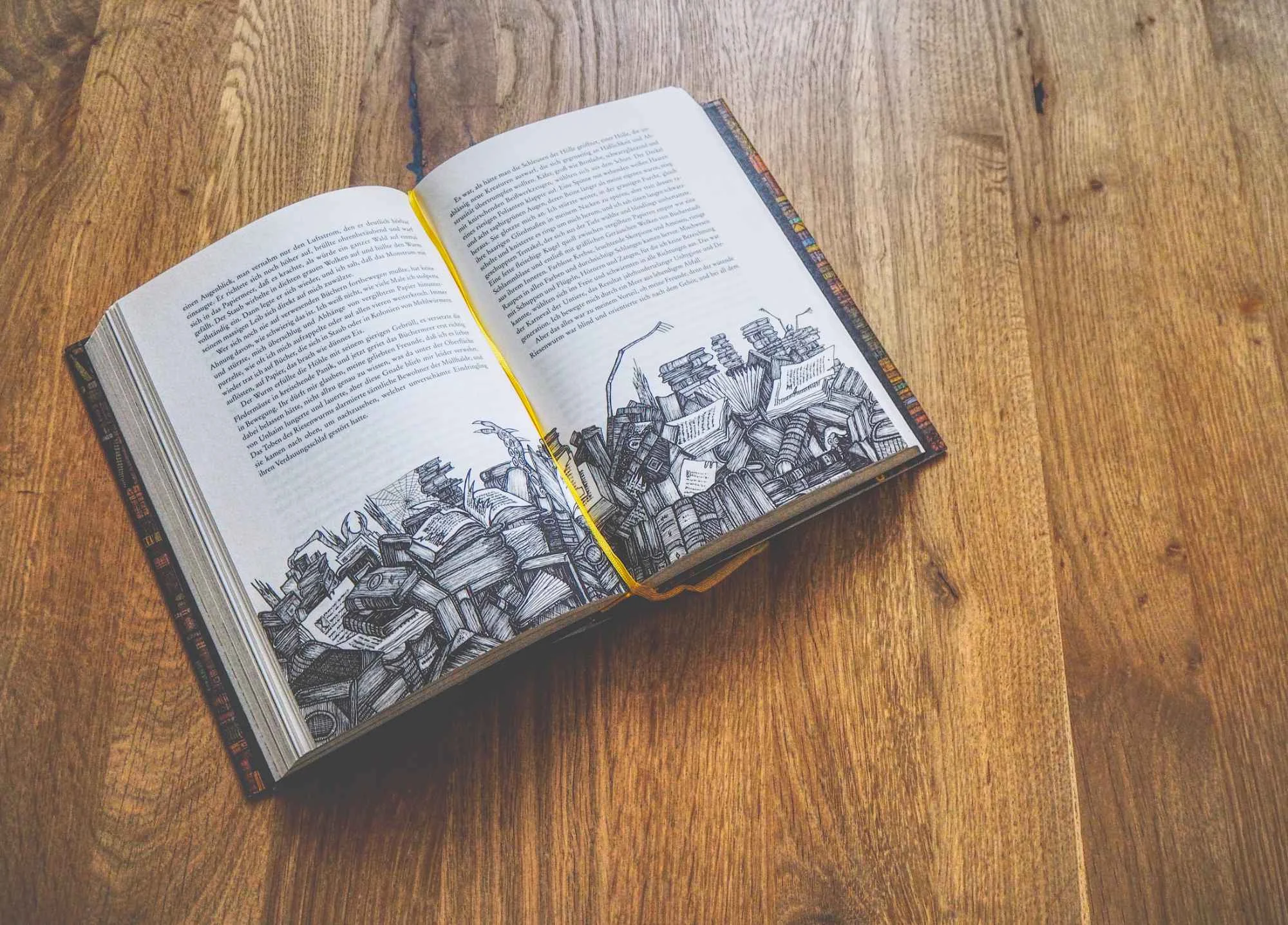 Ein aufgeschlagenes Buch mit Schwarz-Weiß-Abbildungen von gestapelten Büchern und Papieren auf einer Holzoberfläche.