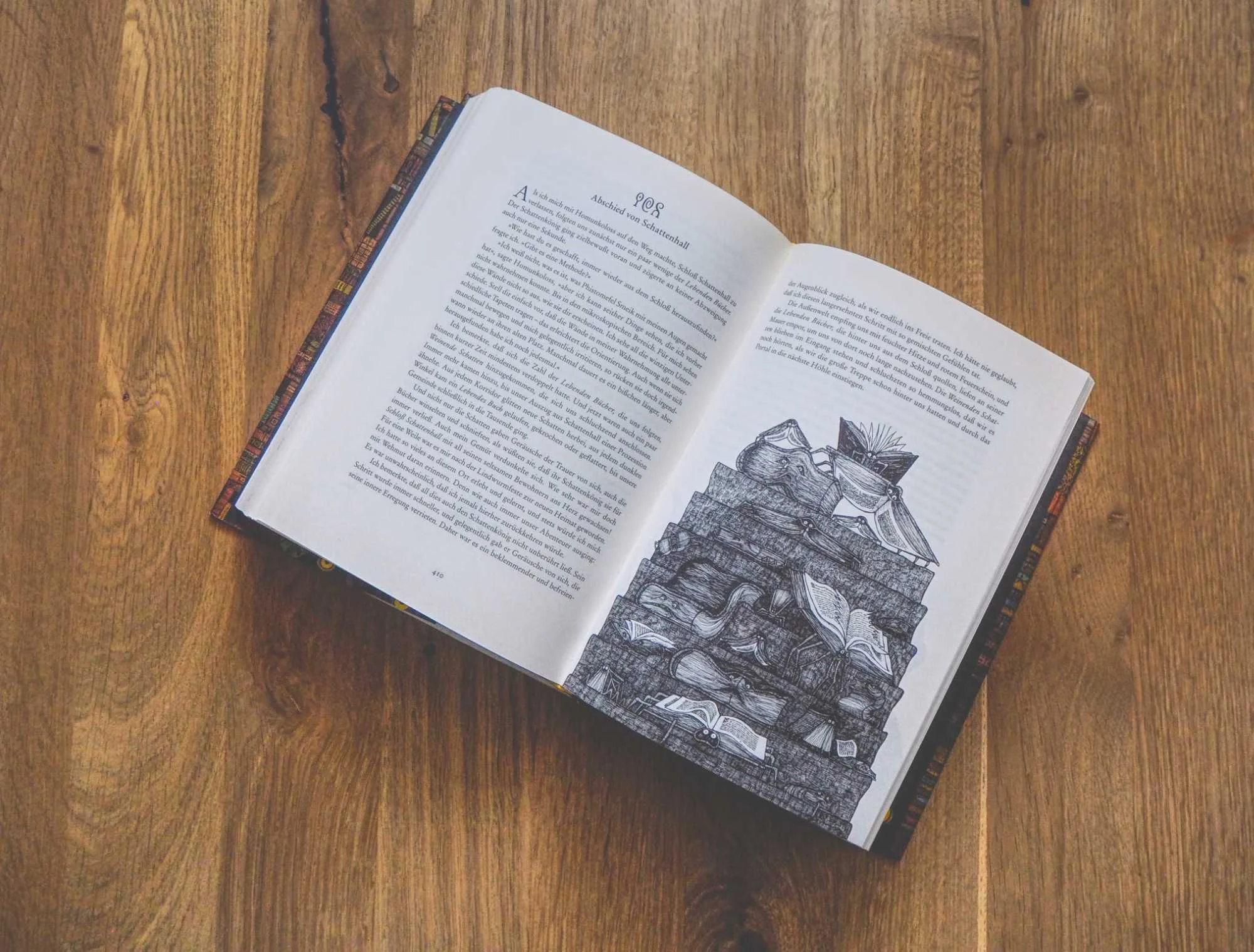 Ein aufgeschlagenes Buch liegt auf einer hölzernen Unterlage und zeigt auf der linken Seite einen Text und auf der rechten Seite die Illustration eines Bücherstapels.