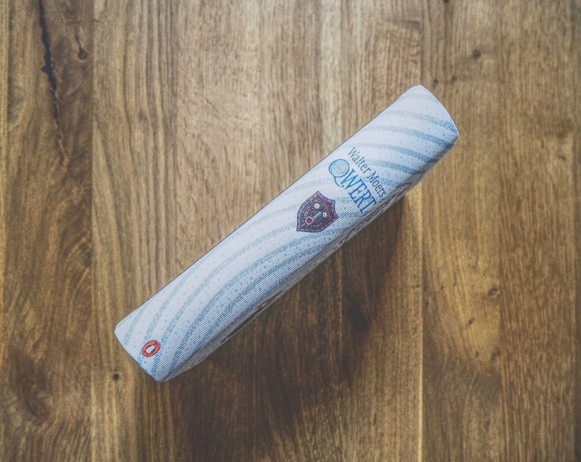 Ein gebundenes Buch mit dem Titel "Qwert" von Walter Moers liegt auf einer hölzernen Unterlage, wobei der Buchrücken von oben betrachtet wird.