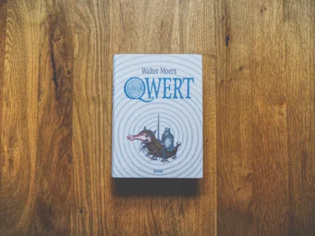 Ein Buch mit dem Titel "Walter Moers QWERT" mit einer illustrierten Kreatur auf dem Einband liegt auf einer Holzfläche.