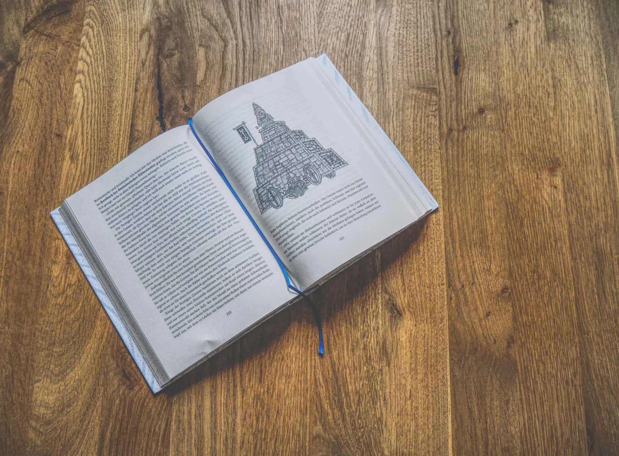 Ein aufgeschlagenes Buch mit einem Text und einer architektonischen Zeichnung wird auf eine Holzfläche gelegt.