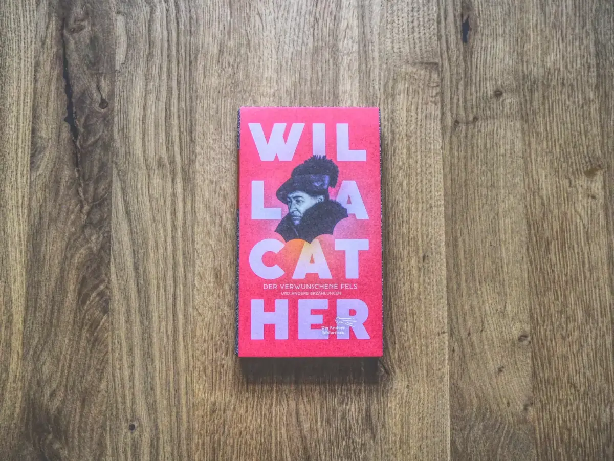 Auf einem Holzboden liegt ein Buch mit dem Titel.