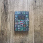 Auf einer Holzplatte liegt das Buch „Die Farbe der Rache“ von Cornelia Funke. Der Einband ist mit bunten, illustrierten Buchstaben verziert.