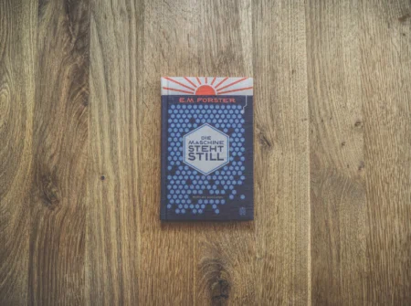 Eine deutsche Ausgabe von E. M. Forsters Buch „Die Maschine steht still“ auf einer Holzoberfläche. Der Einband zeigt ein sechseckiges Muster und den Titel in fetten Buchstaben.