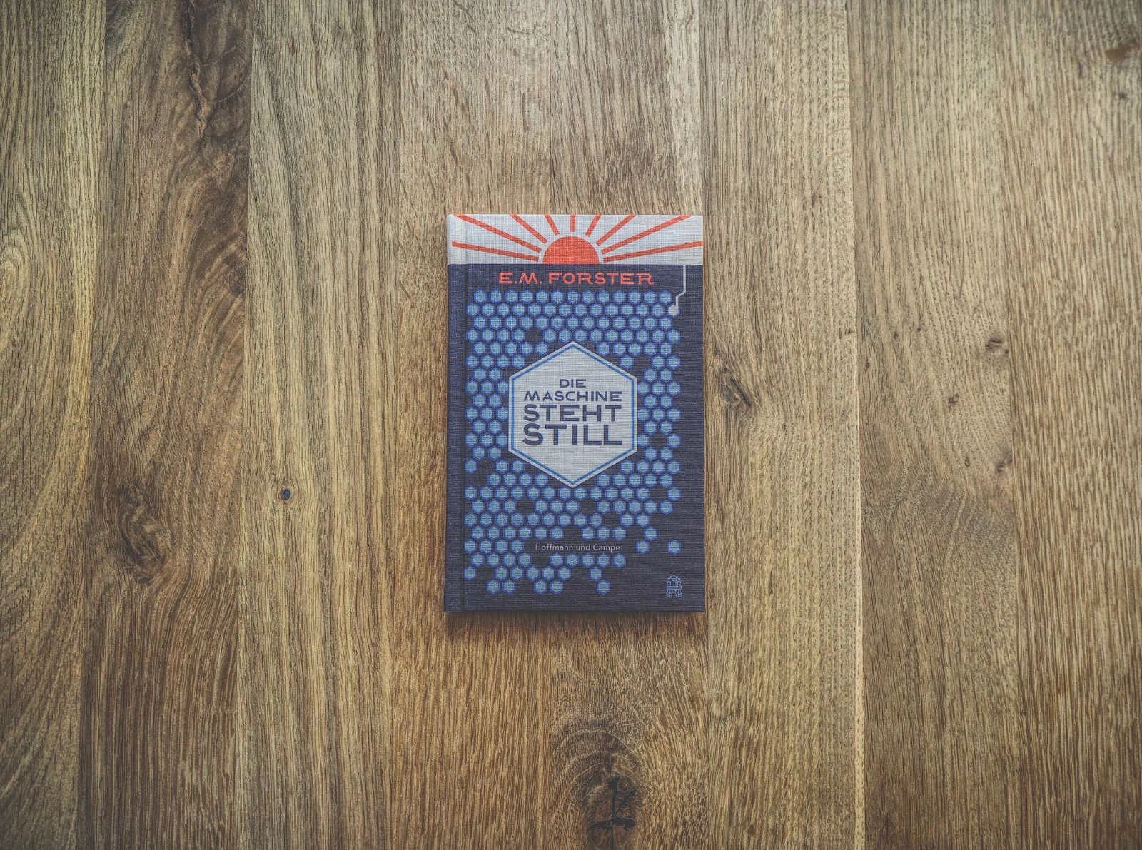 Eine deutsche Ausgabe von E. M. Forsters Buch „Die Maschine steht still“ auf einer Holzoberfläche. Der Einband zeigt ein sechseckiges Muster und den Titel in fetten Buchstaben.