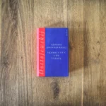 Auf einer Holzfläche liegt ein Buch mit dem Titel „Verbrechen und Strafe“ von Fjodor Dostojewskij. Das Buch hat einen rot-blauen Einband.