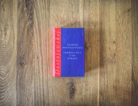 Auf einer Holzfläche liegt ein Buch mit dem Titel „Verbrechen und Strafe“ von Fjodor Dostojewskij. Das Buch hat einen rot-blauen Einband.