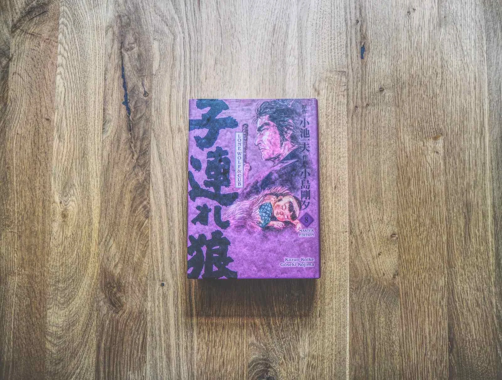 Ein japanisches Buch mit lilafarbenem Einband und illustrierten Schriftzeichen liegt auf einer Holzfläche.