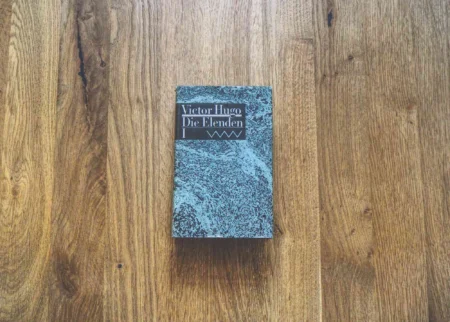 Ein Exemplar von Victor Hugos "Die Elenden" liegt geschlossen auf einer Holzplatte.