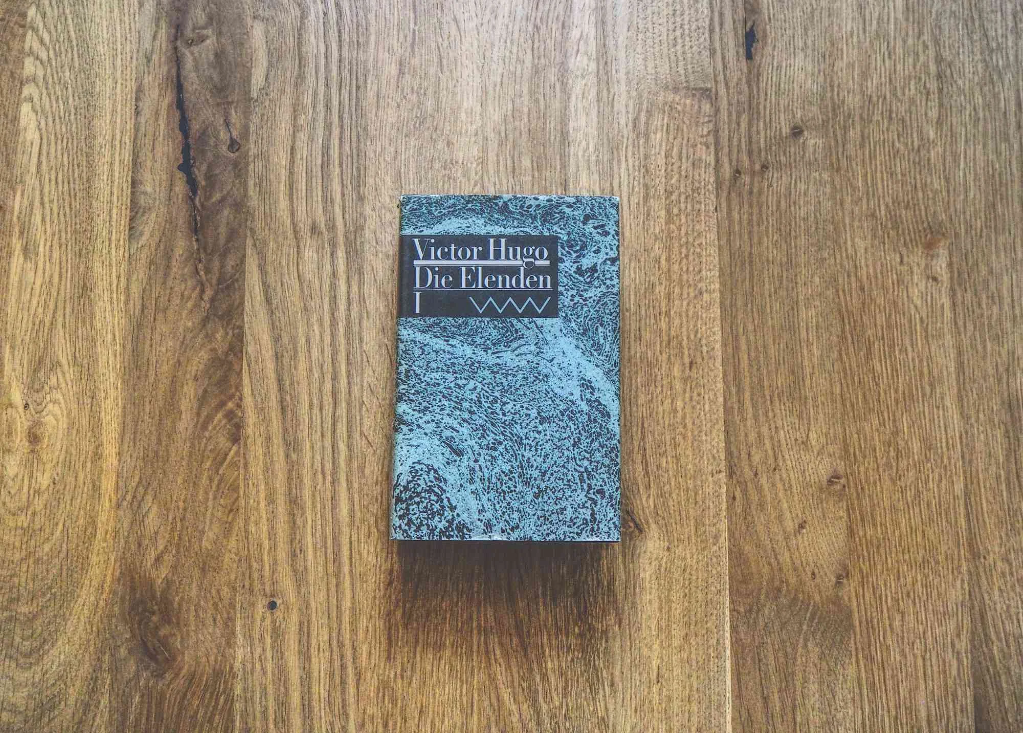 Ein Exemplar von Victor Hugos "Die Elenden" liegt geschlossen auf einer Holzplatte.
