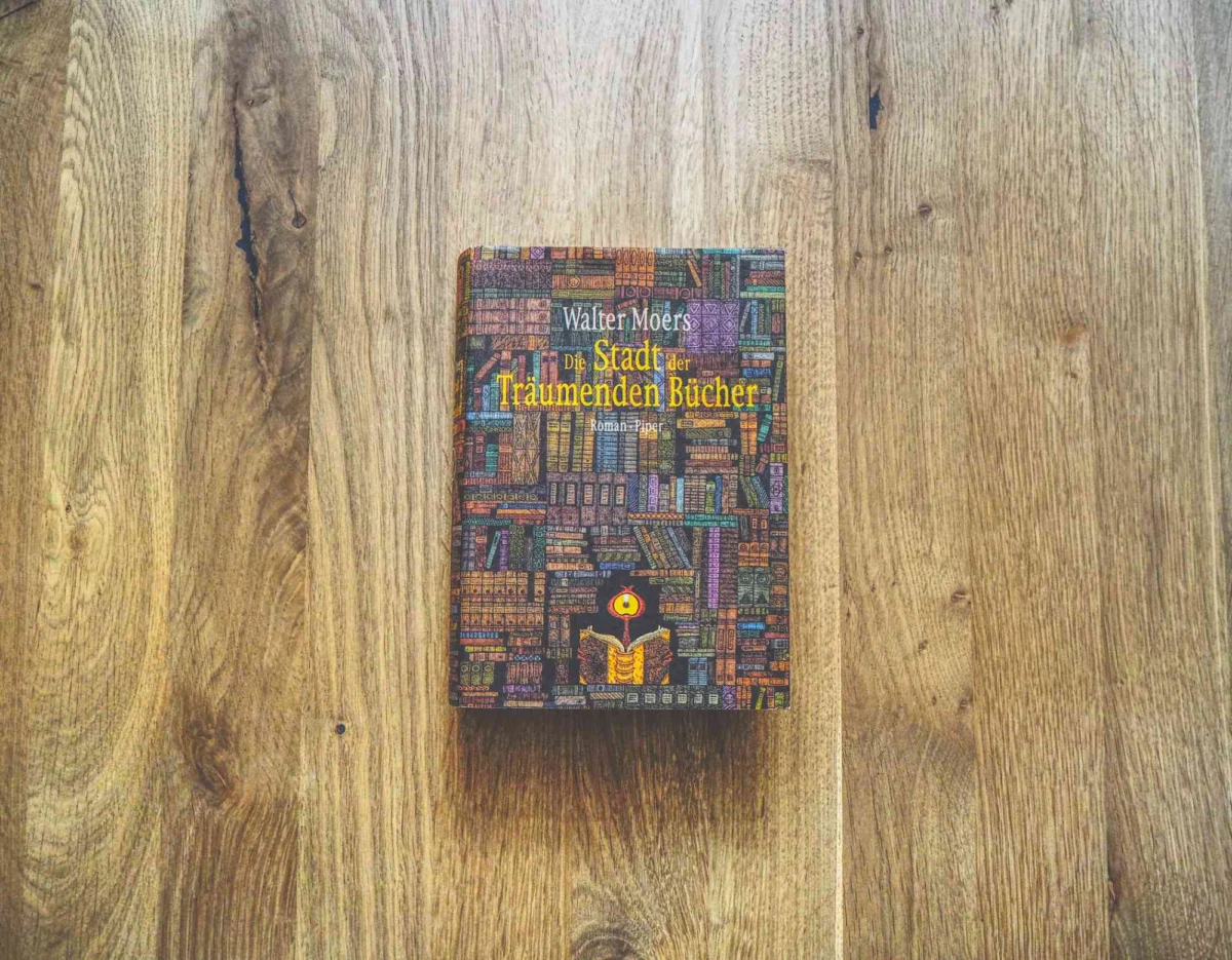 Ein gebundenes Buch mit dem Titel "Die Stadt der Träumenden Bücher" von Walter Moers liegt auf einer hellen Holzfläche.